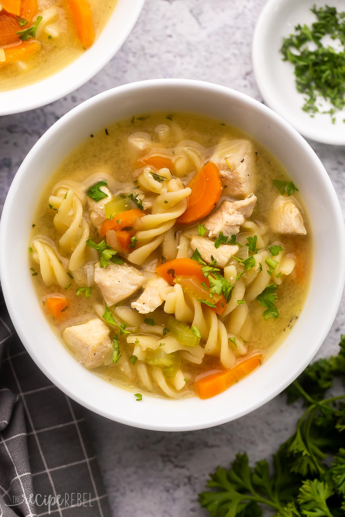 white bowl full of turkey noodle soup on grey surface with parsley beside.