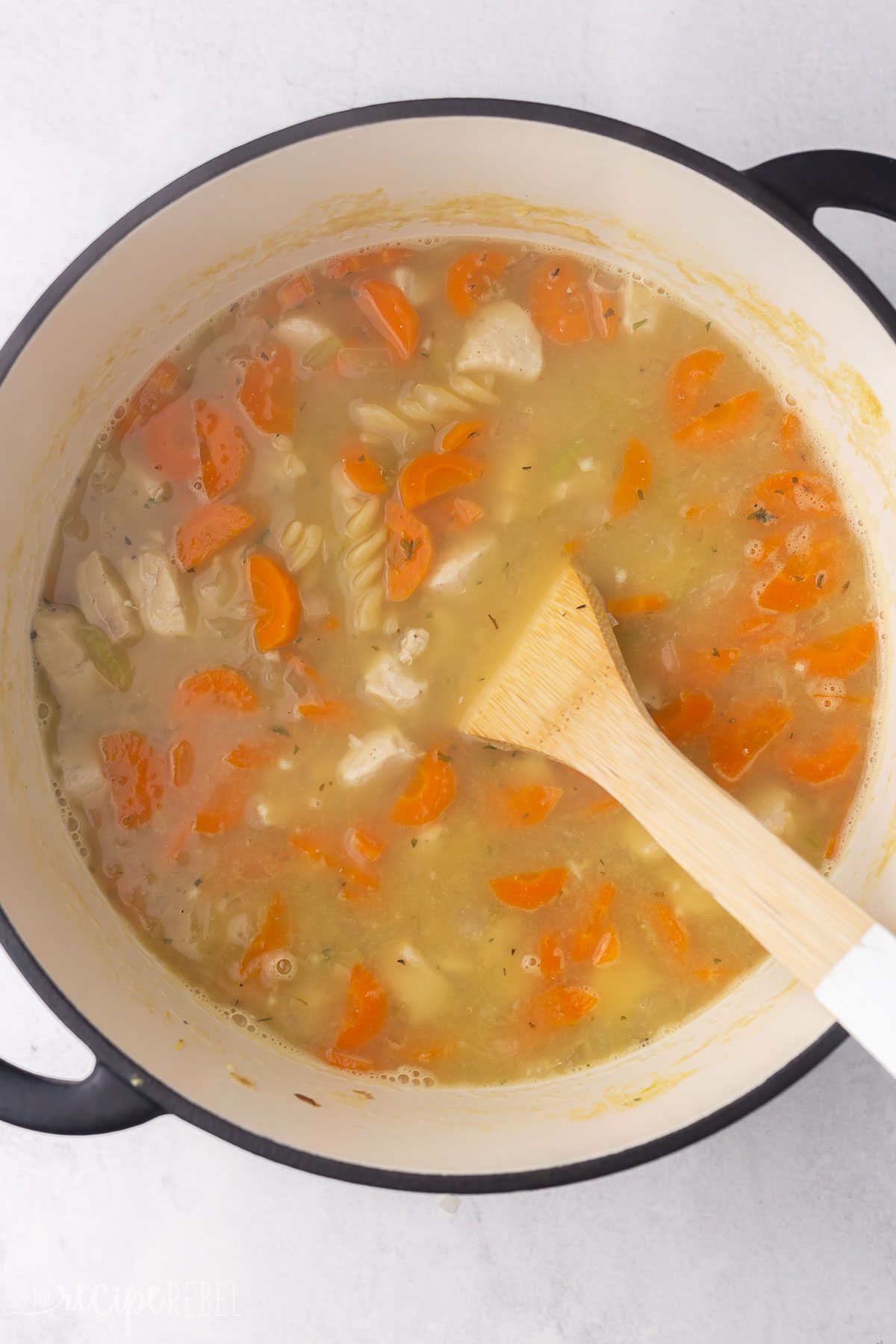 cooked turkey noodle soup in black pot with wooden ladle.