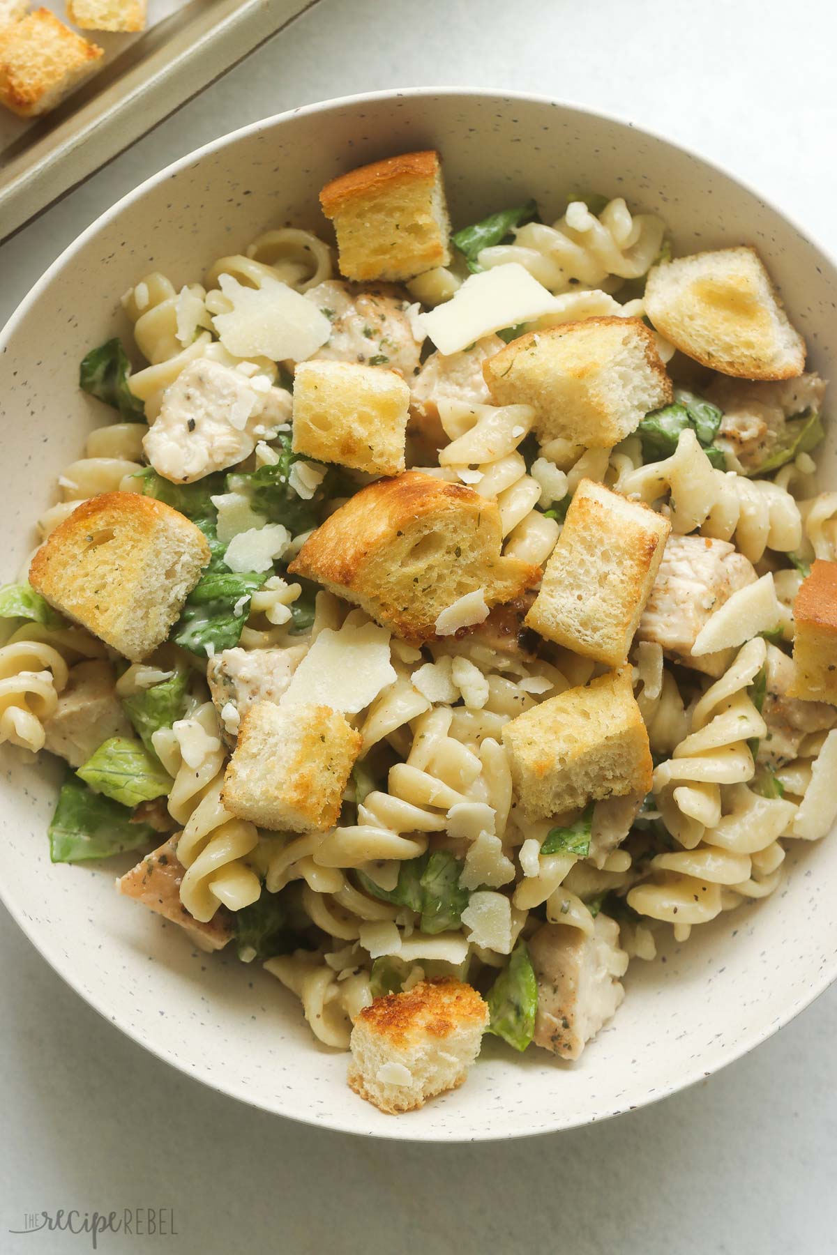 This Chicken Caesar Pasta Salad is made with seasoned chicken breast, rotini pasta, Caesar dressing, Parmesan and garlic bread croutons. It's a light but still hearty summer meal, perfect for picnics! #salad #recipe #dinner | pasta salad recipes | chicken pasta salad | caesar salad | rotini | barbecue sides | picnic food | summer recipes | cookout recipes close up image of chicken caesar pasta salad in a bowl.