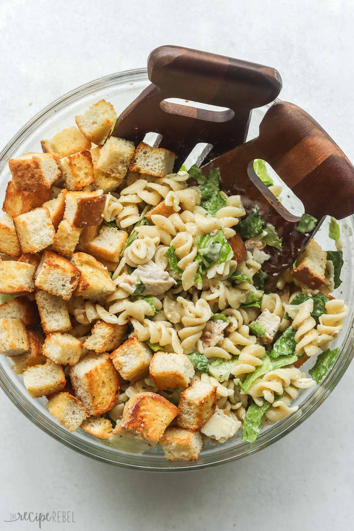 overhead image of chicken caesar pasta salad in a glass bowl with croutons on top.