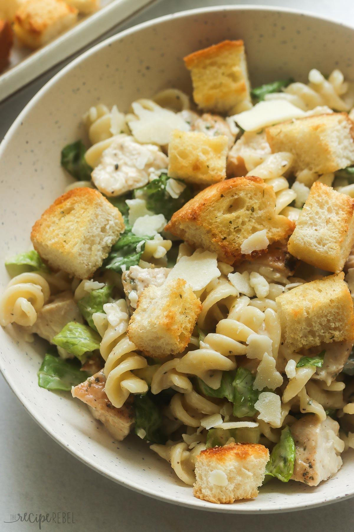 close up image of caesar pasta salad with chicken and rotini pasta in a bowl with croutons.