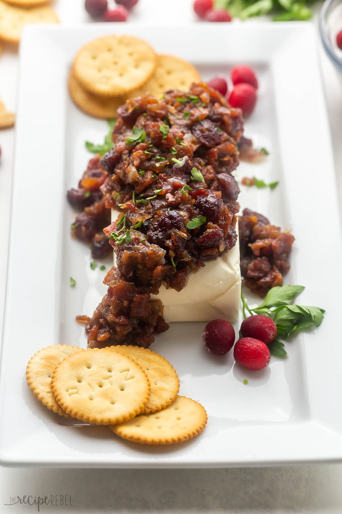 cranberry bacon cream cheese appetizer on a white plate with crackers and cranberries around.