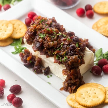 platter with cream cheese block covered in cranberry bacon sauce and crackers arranged around.