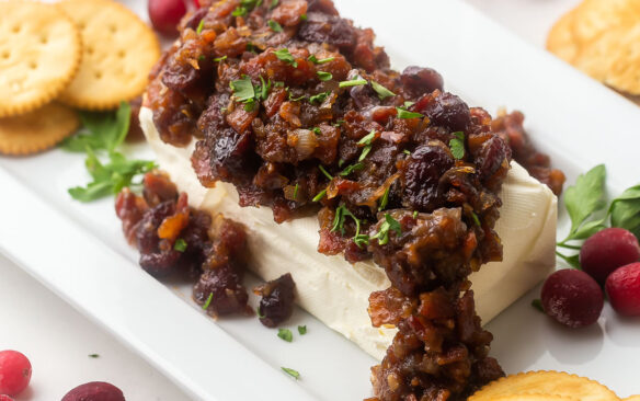 platter with cream cheese block covered in cranberry bacon sauce and crackers arranged around.