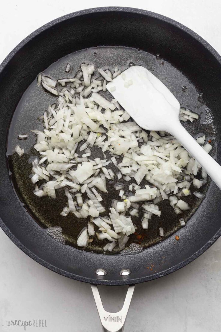 chopped onions in black frying pan and white spatula.