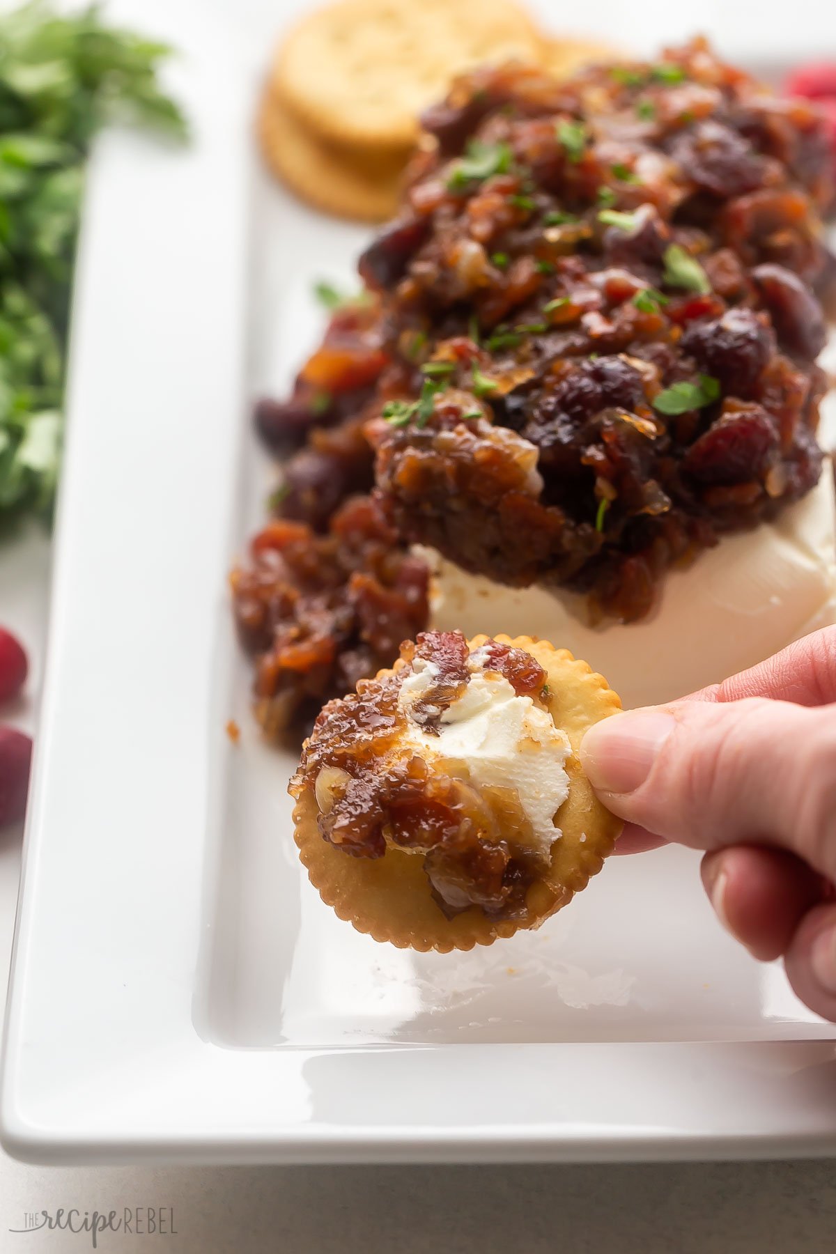 a hand holding a cracker with cranberry bacon cream cheese on it.