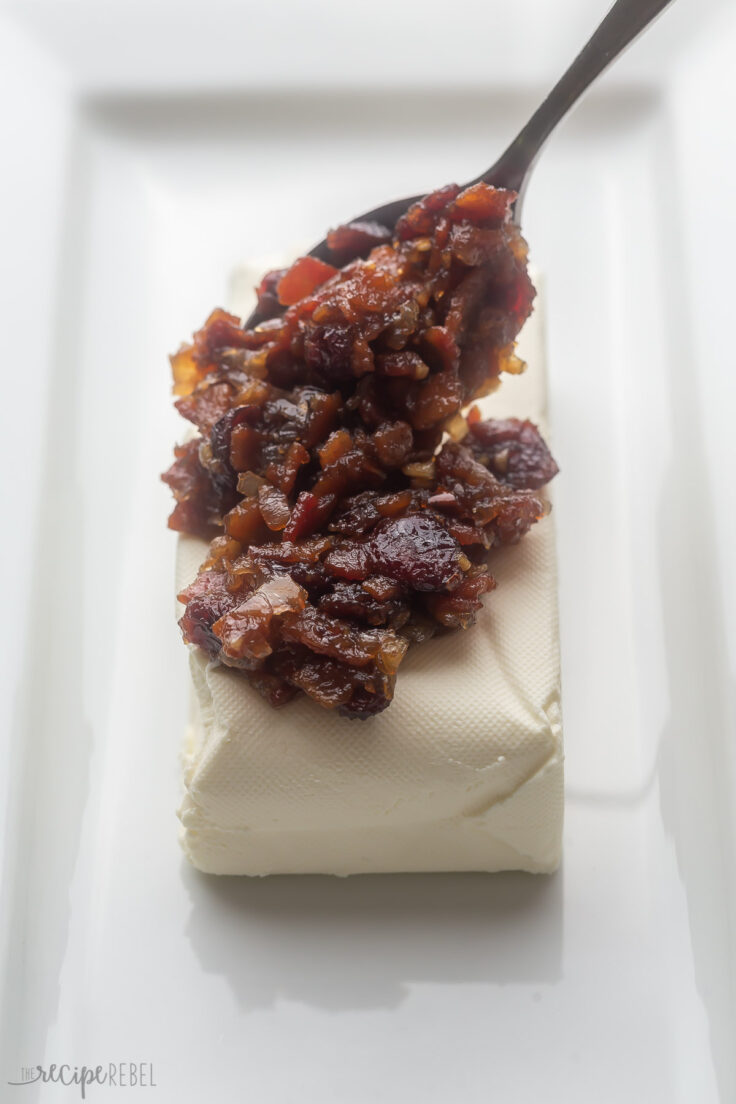 cranberry bacon sauce being set on top of cream cheese.