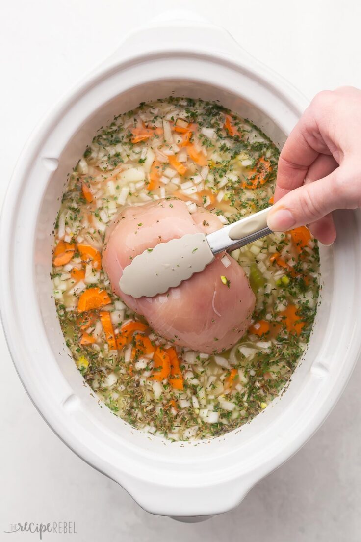 overhead of a chicken breast being placed into white crockpot.