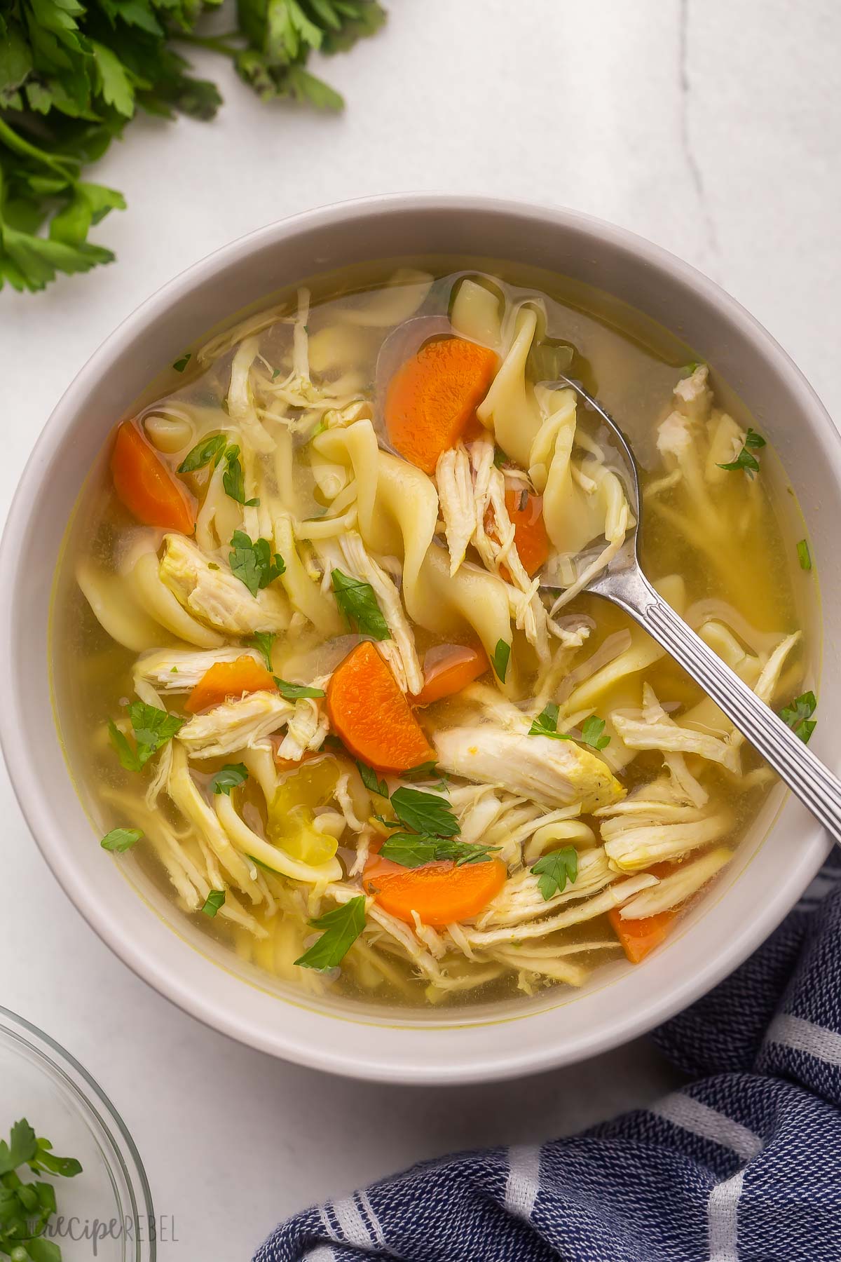 chicken noodle soup in grey bowl with spoon and chopped parsley.