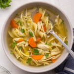 close up of spoon and bowl of chicken noodle soup.