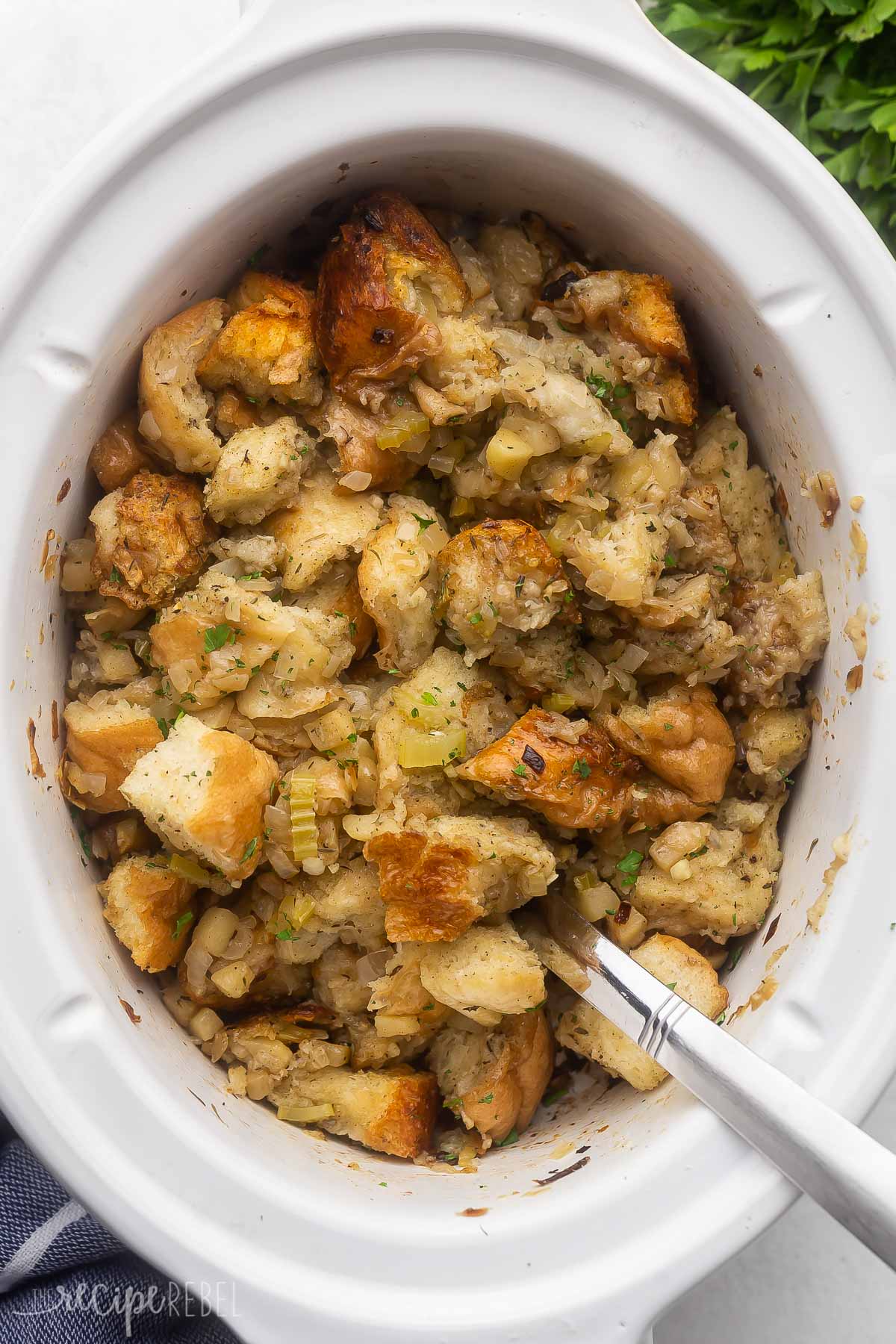 overhead view of a white crockpot filled with stuffing and a steel ladle.