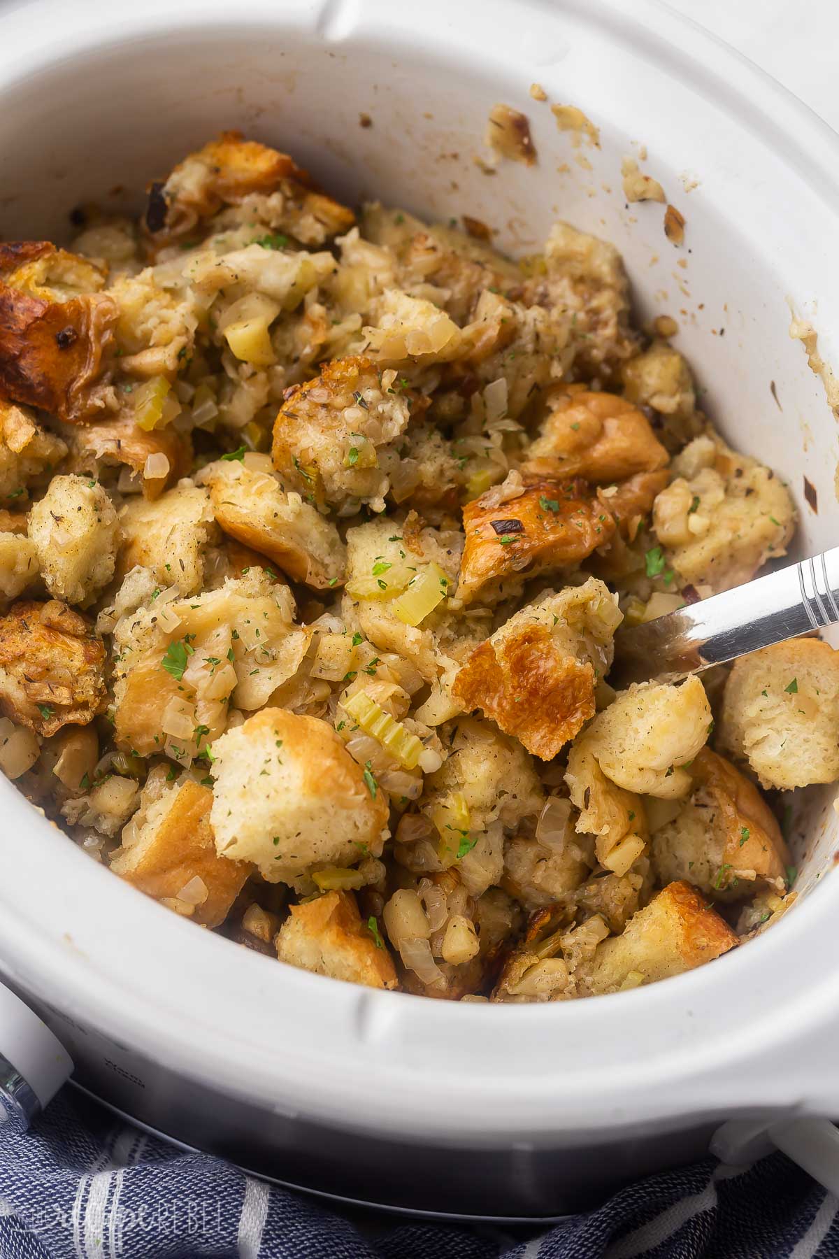 white crockpot full of stuffing and steel scoop.