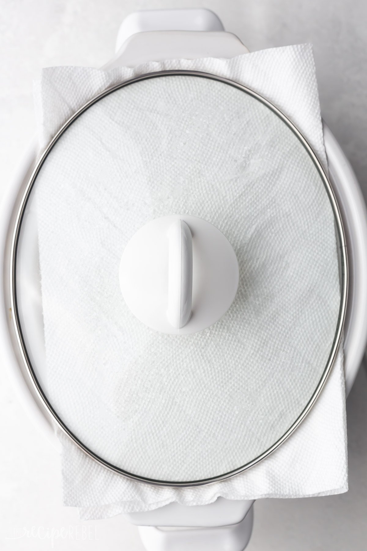 white crockpot with paper towel on top and covered with a glass lid.