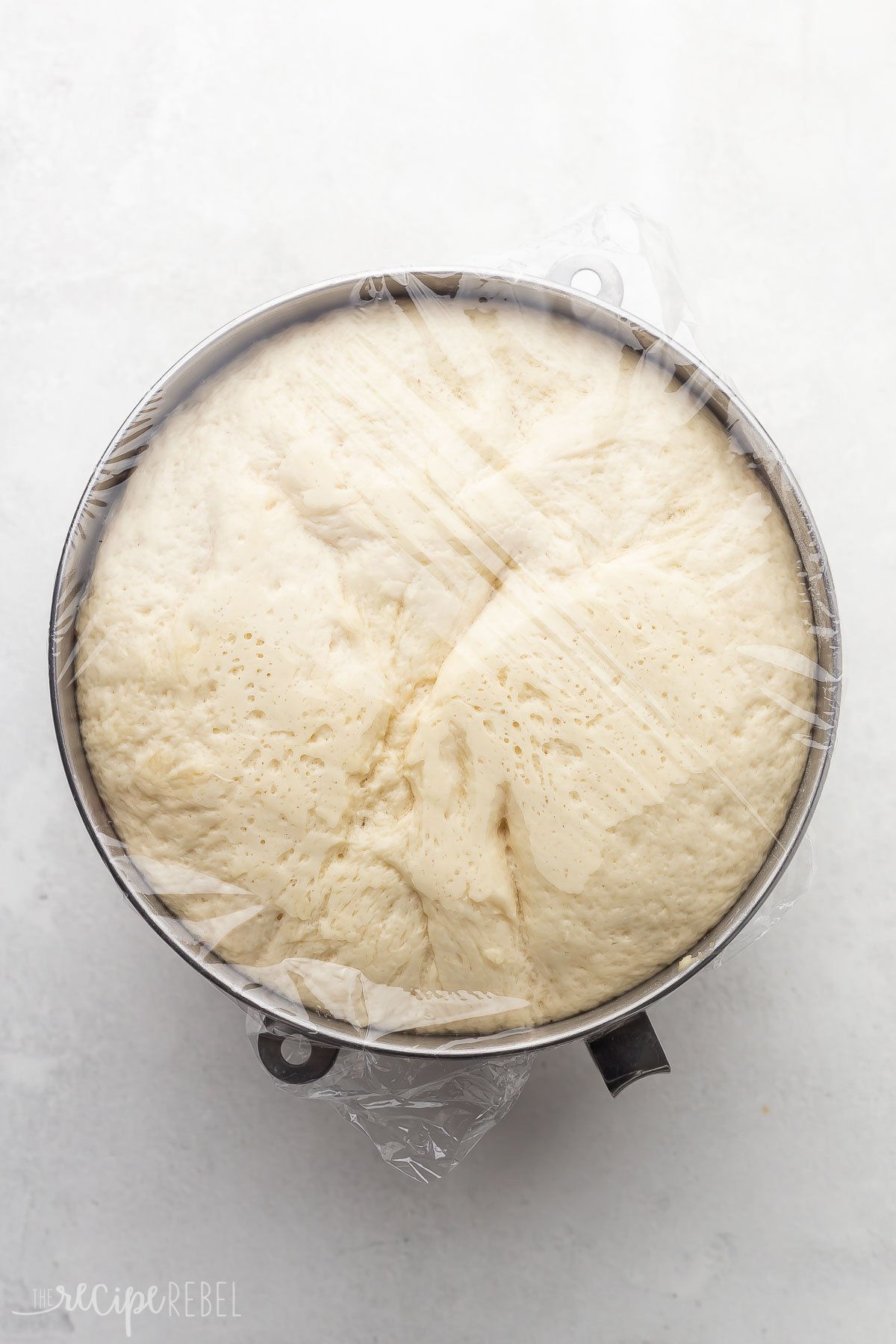 risen dough in mixing bowl covered with plastic wrap.