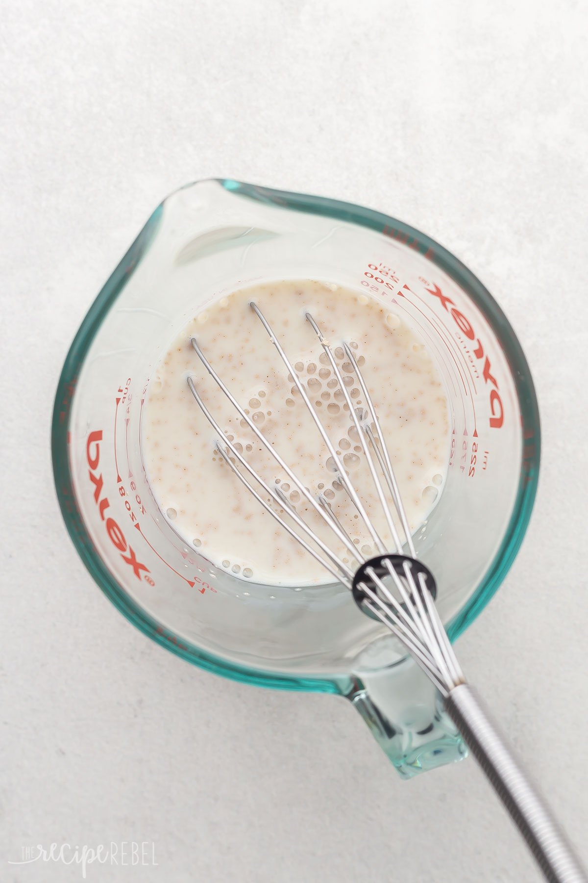 glass measuring cup with yeast mixture and steel whisk in it.