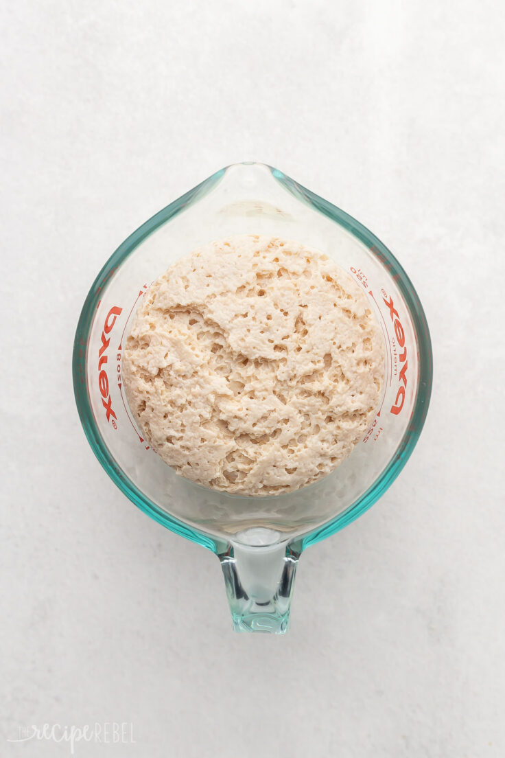 glass measuring cup with risen yeast on grey surface.