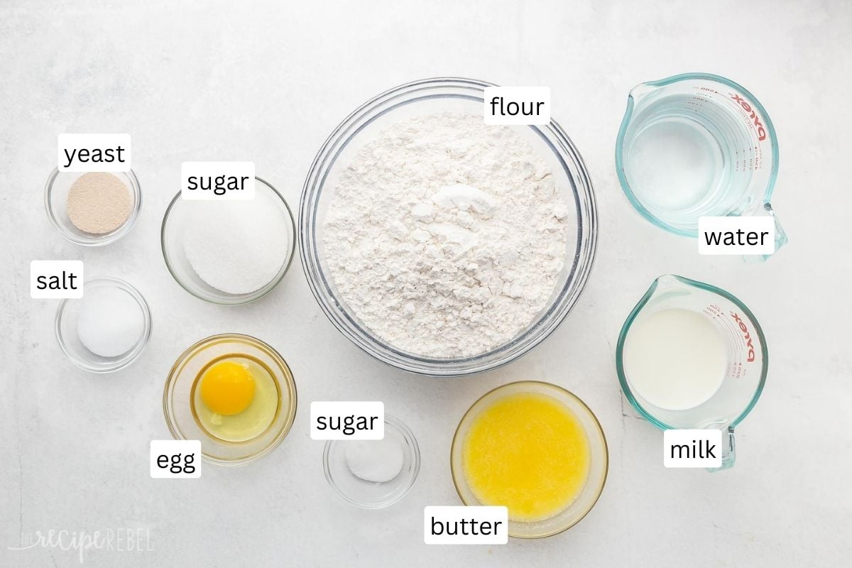 ingredients for homemade dinner rolls in glass bowls on white surface.