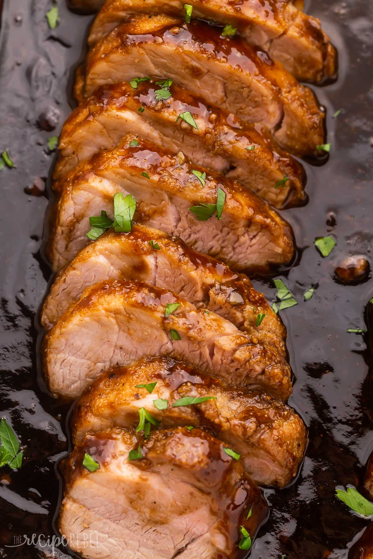 close up of sliced pork tenderloin in sauce garnished with chopped parsley.