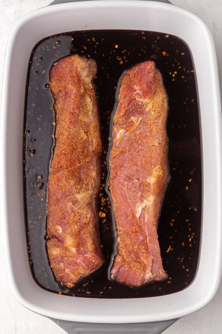 pork tenderloin lying in honey balsamic sauce in a baking dish.