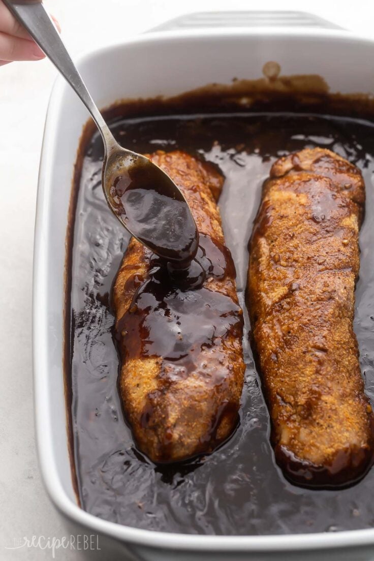 baked pork tenderloin in a dish with a spoon drizzling sauce on top.