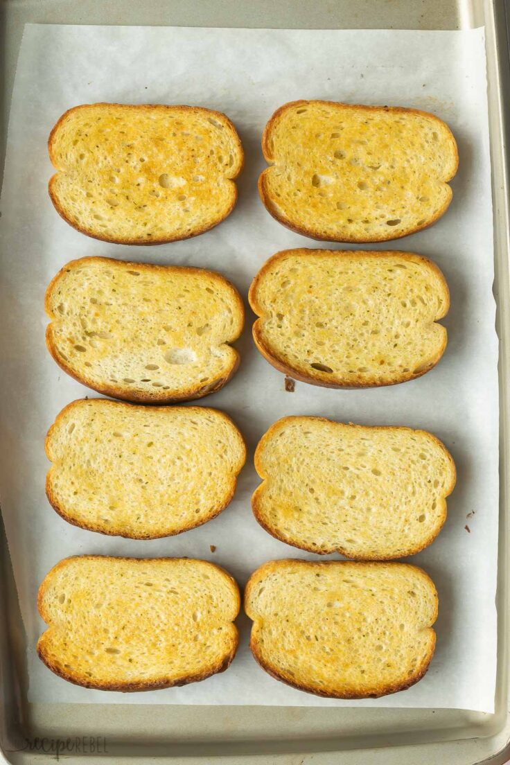 toasted garlic bread slices on parchment lined baking sheet.