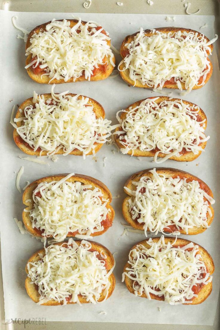 cheese on top of sauce on garlic bread on a baking sheet.