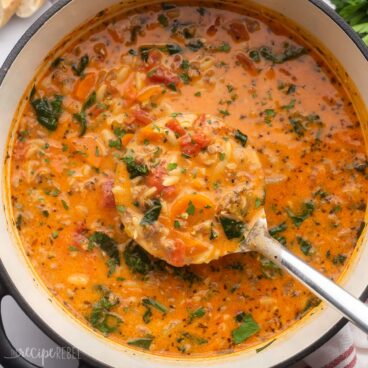 overhead view of pot of sausage orzo soup with steel ladle in.