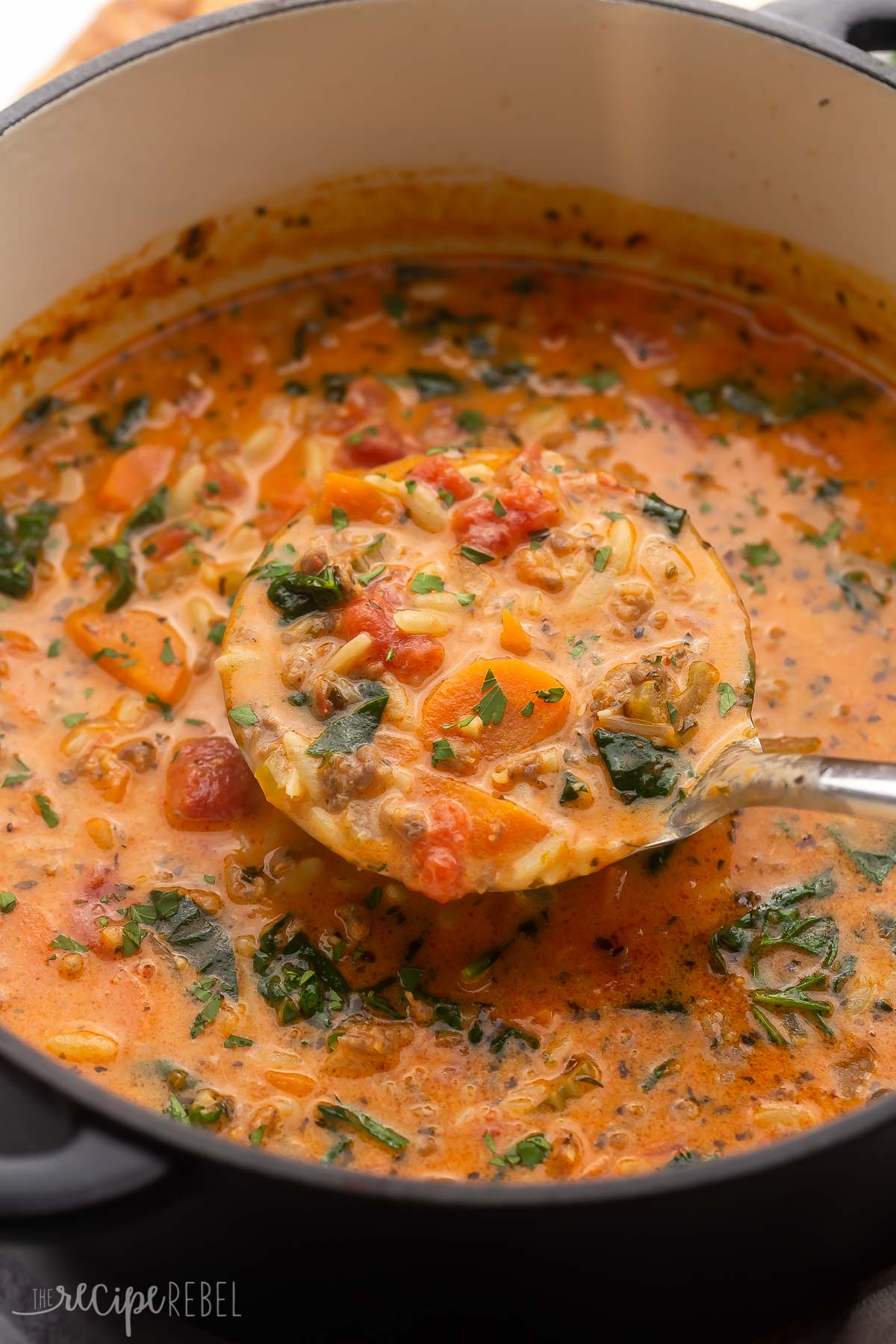 close up of a ladle of sausage orzo being scooped out of pot.