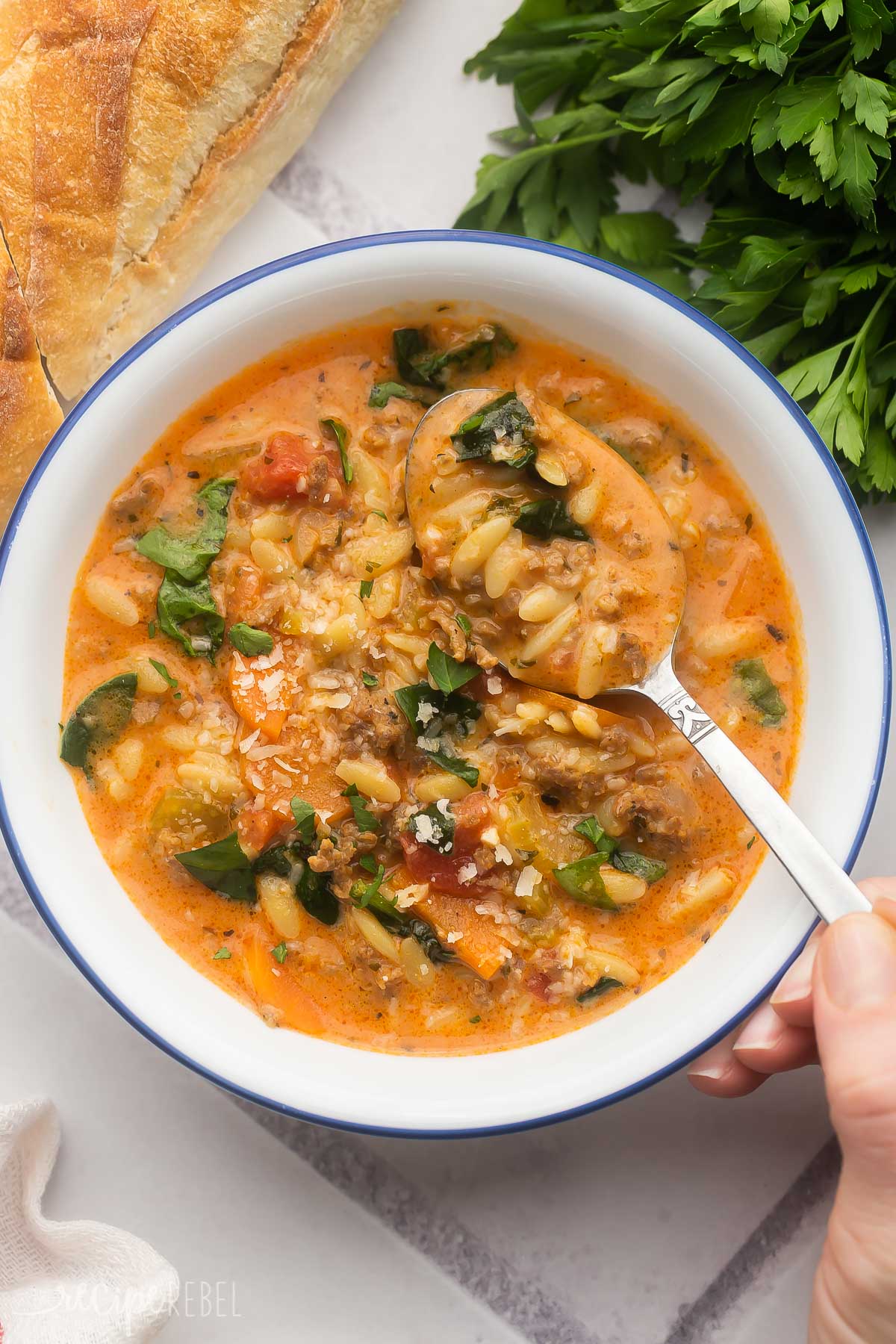 white bowl filled with sausage orzo soup and a spoon scooping some out.