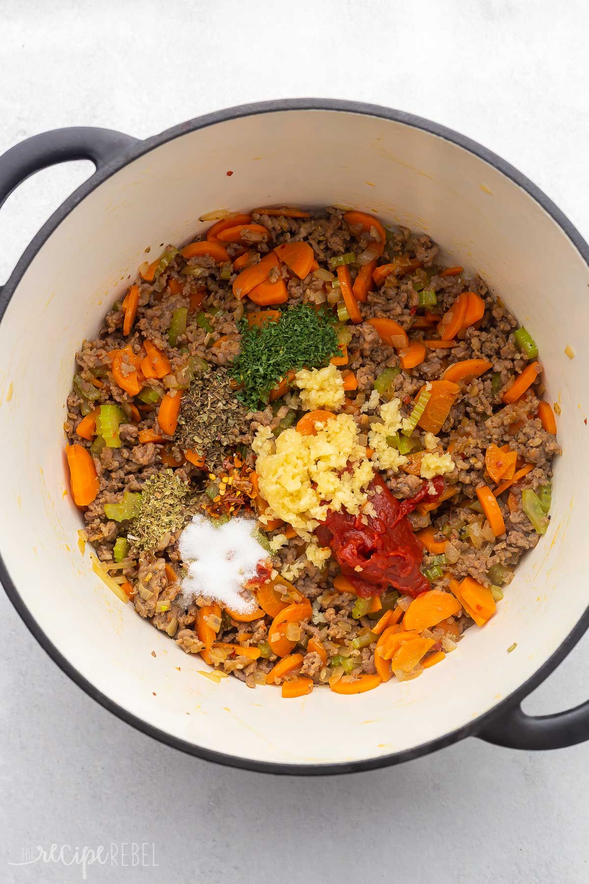 dutch oven with cooked vegetables, meat, and spices added.