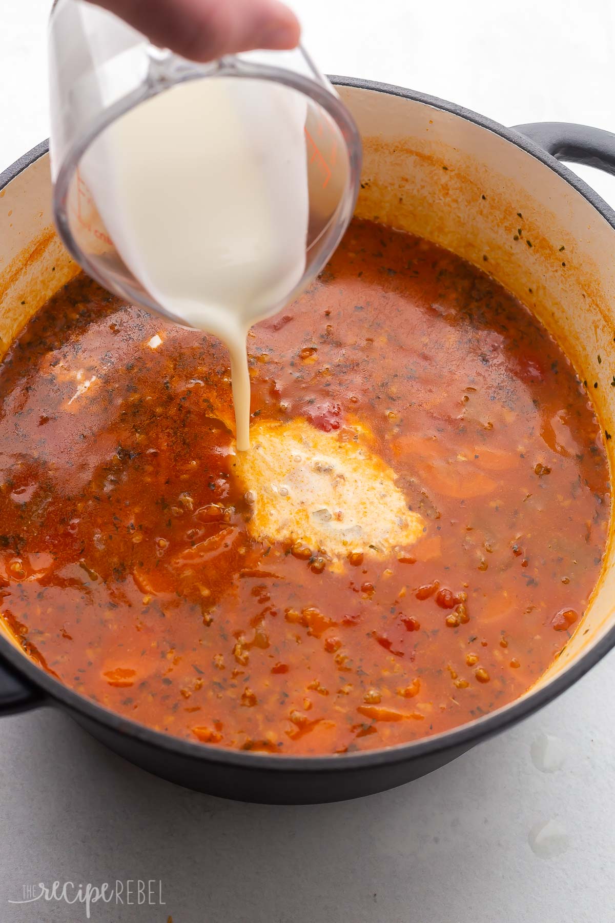 pouring cream into pot of sausage orzo soup.