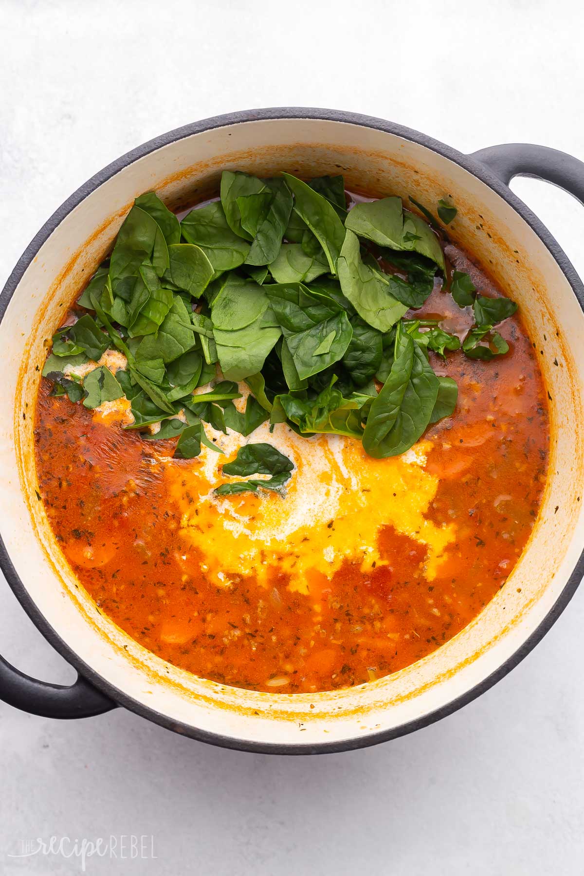 large dutch oven full of soup with chopped spinach added on top.