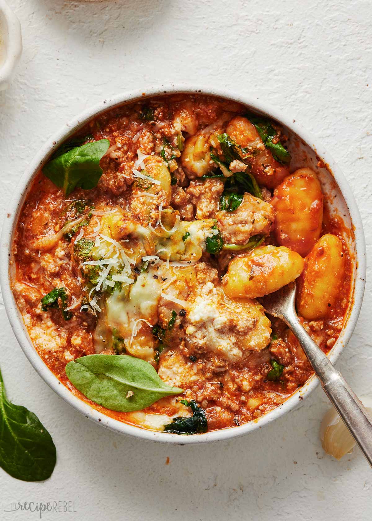 full bowl of three cheese gnocchi bake with a spoon in on a white surface.