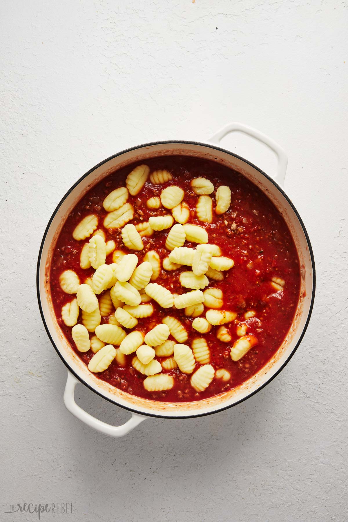 white dutch oven with cooked sauce and gnocchi added on top.