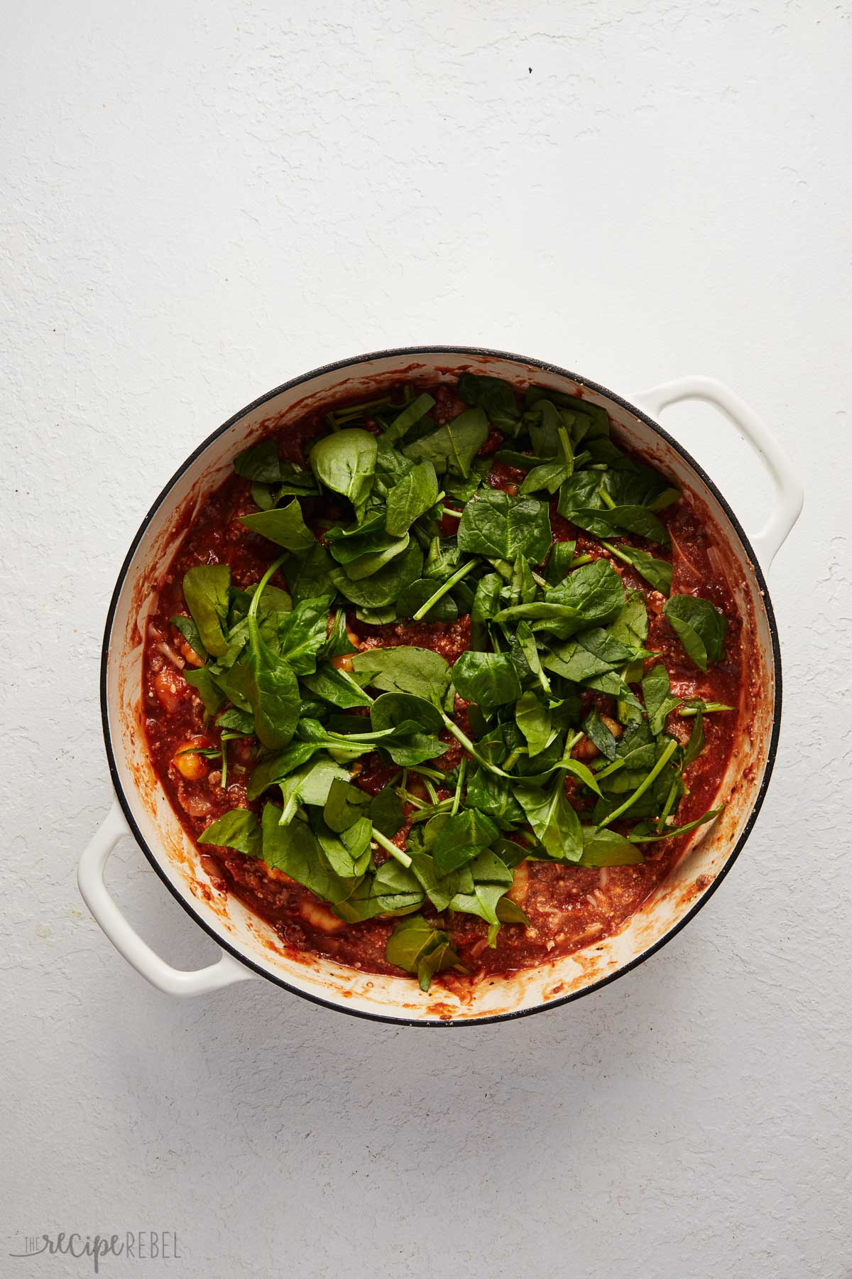 fresh spinach added to pot of sauce mixture in white dutch oven.