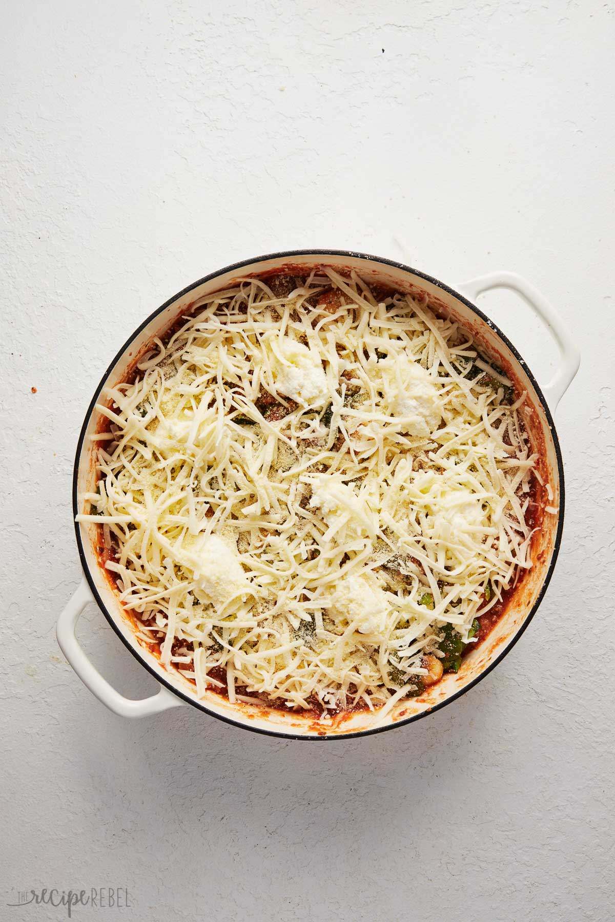 white dutch oven with gnocchi bake inside and shredded cheese added on top.