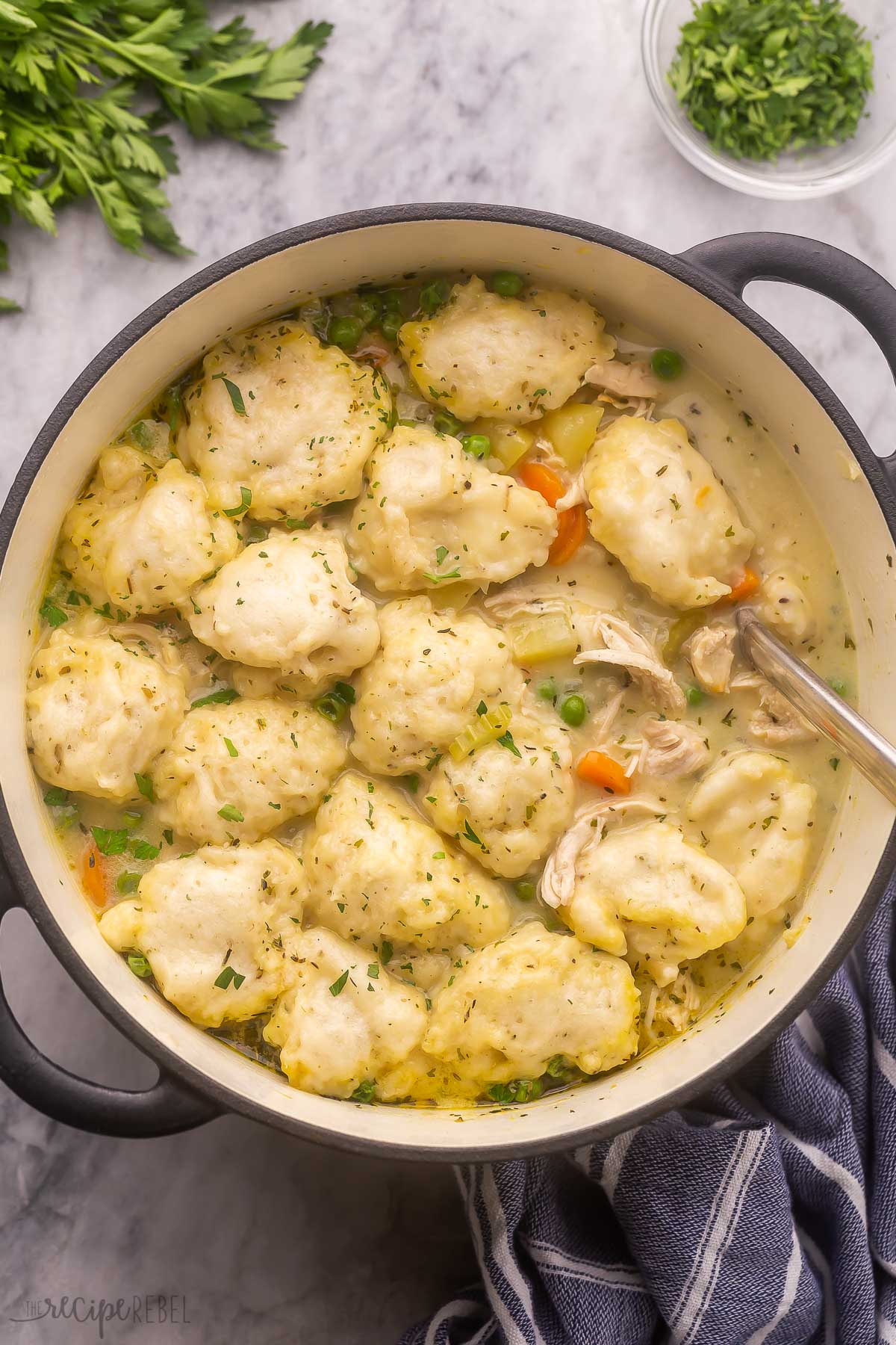 overhead view of a large black pot filled with chicken dumpling soup on grey surface.