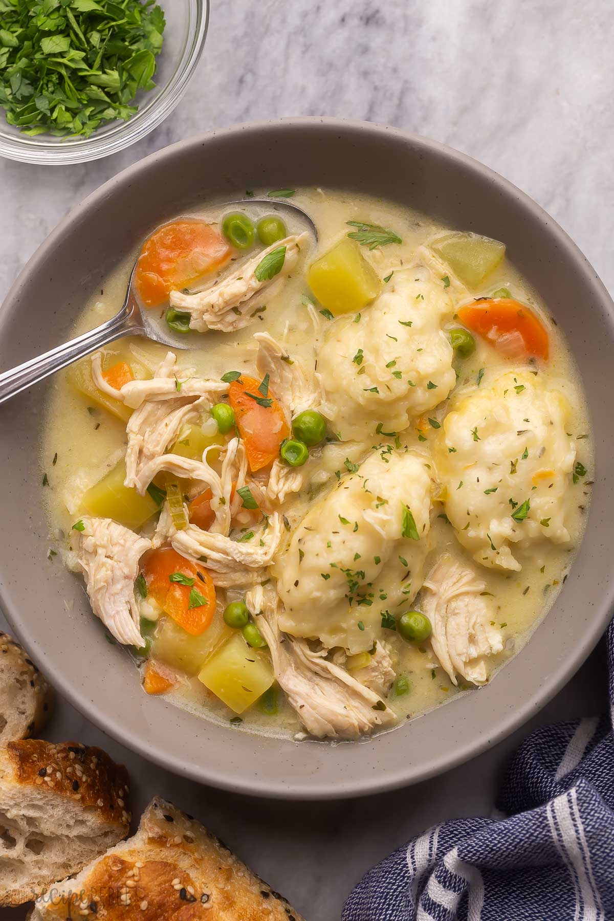 overhead of a spoon in a grey bowl filled with chicken dumpling soup.