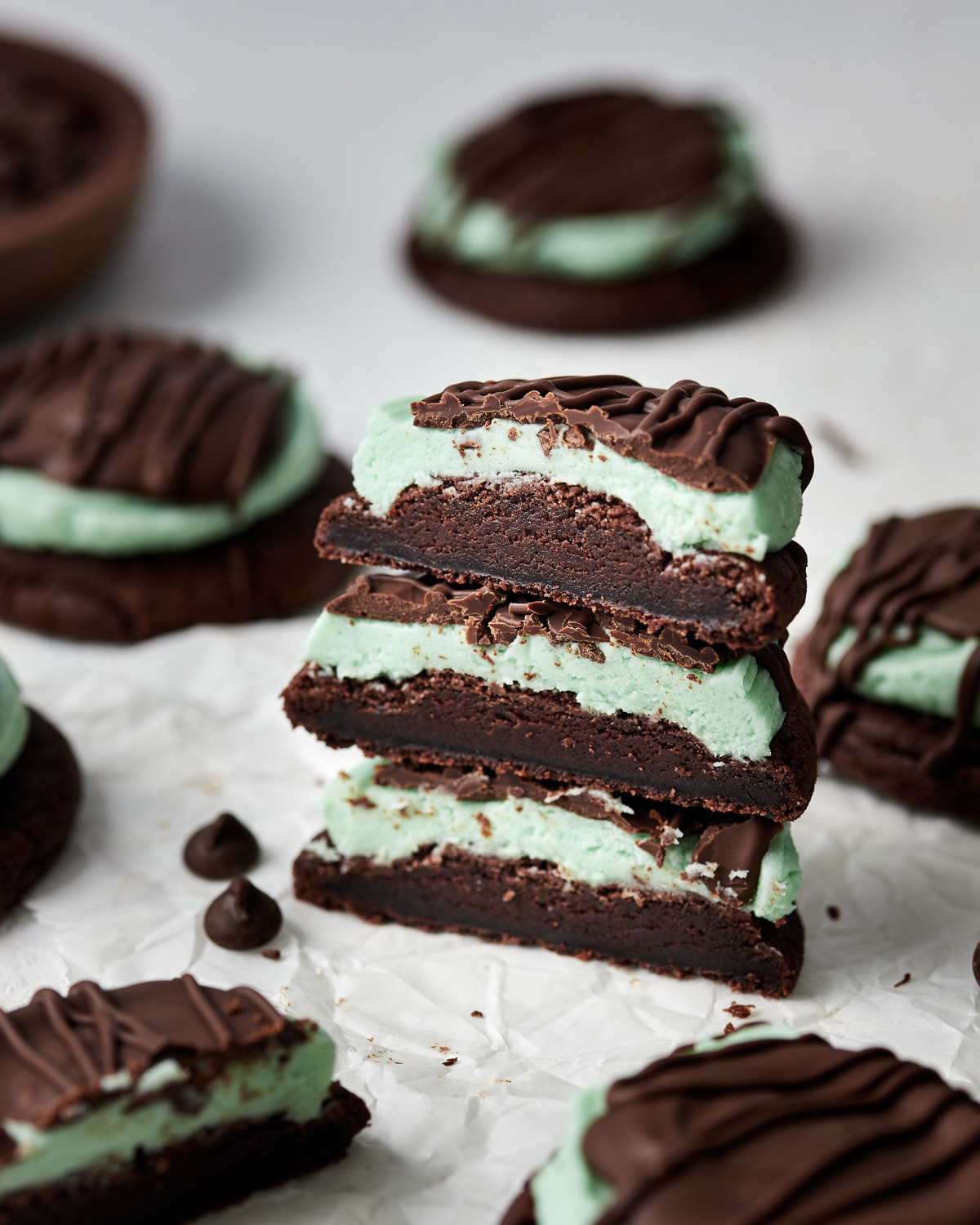 halved chocolate mint cookies stacked up with chocolate chips beside.