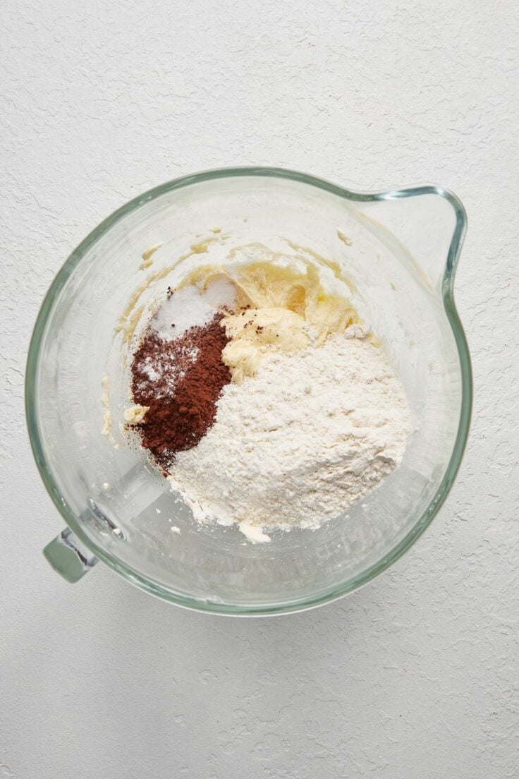 flour and cocoa on top of mixed ingredients in a glass mixing bowl.
