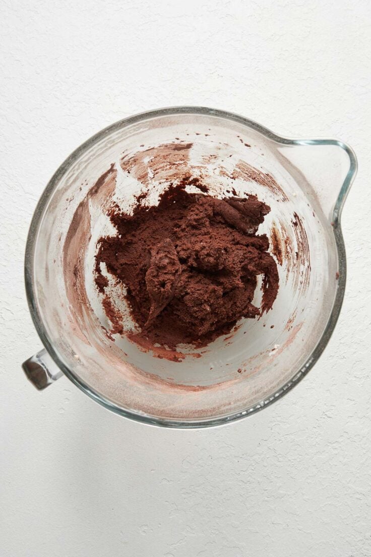 chocolate mixed ingredients in glass mixing bowl on white surface.