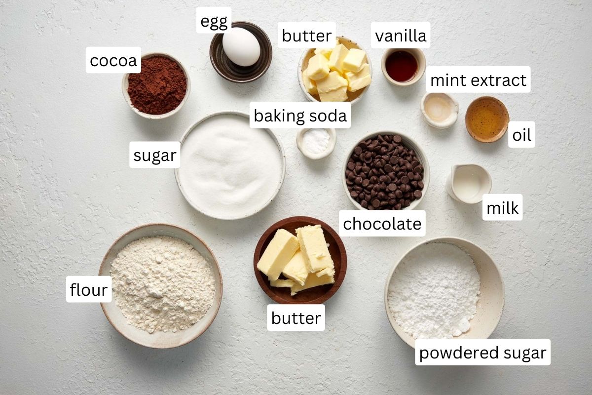 ingredients for chocolate mint cookies in bowls on white surface.