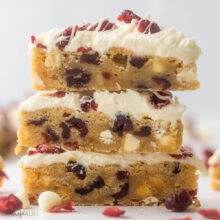 close up of a stack of cranberry bliss bars with chocolate chips and cranberries beside.
