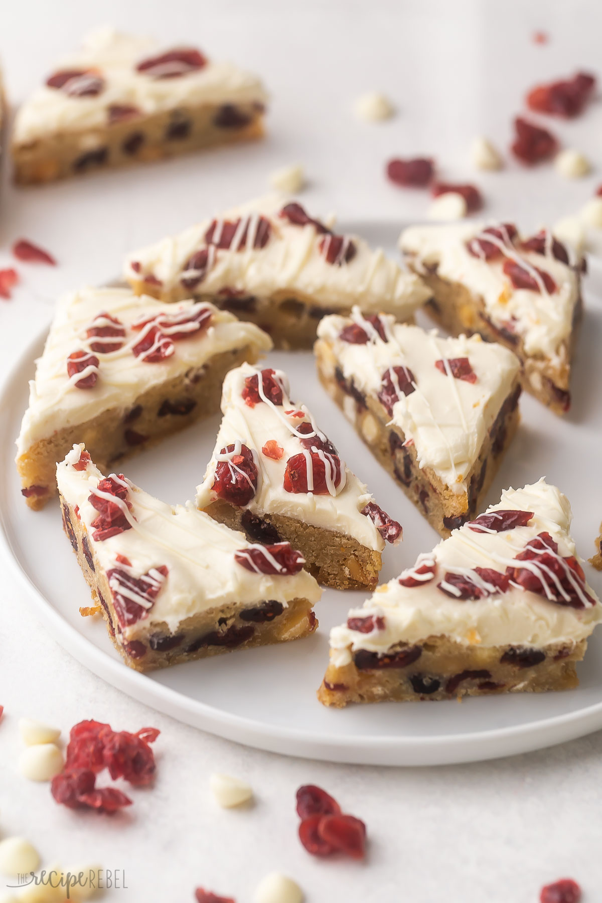 white plate filled with cranberry bliss bars with cranberries in foreground.