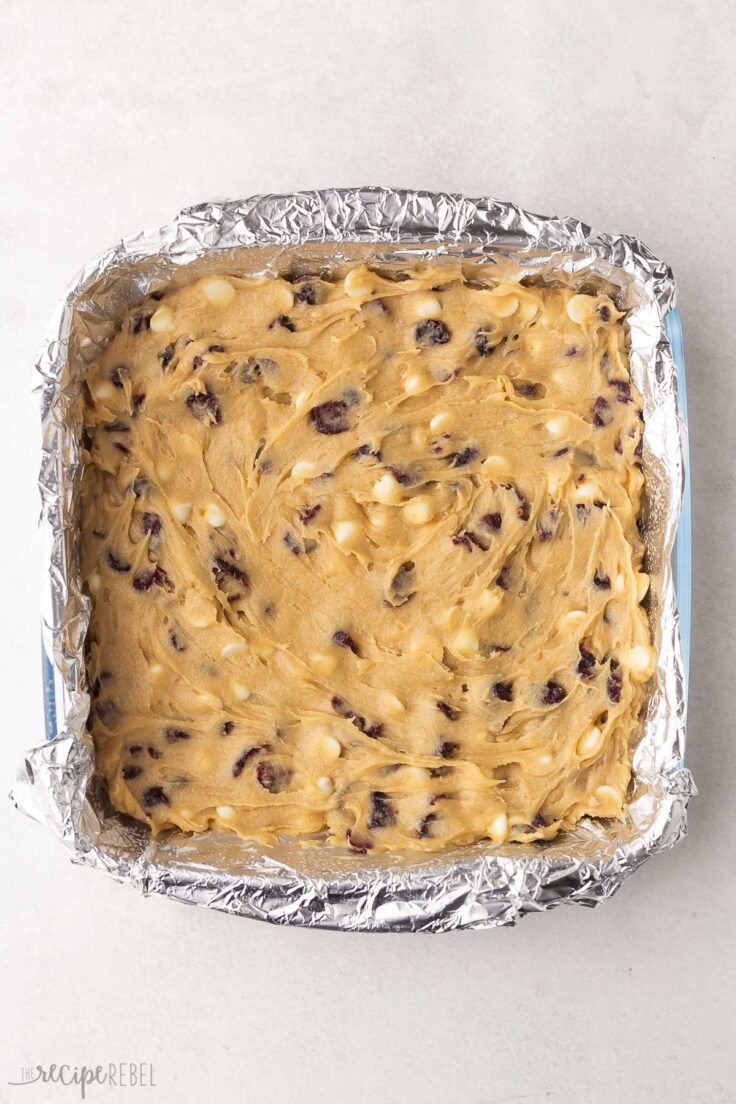 cranberry bliss bars spread in tinfoil lined pan ready to be baked.