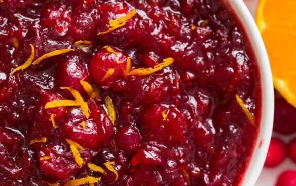 homemade cranberry sauce in white bowl with orange zest on top.