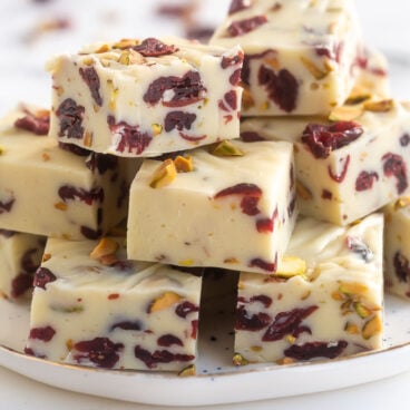 pieces of cranberry white chocolate fudge stacked on a white plate.