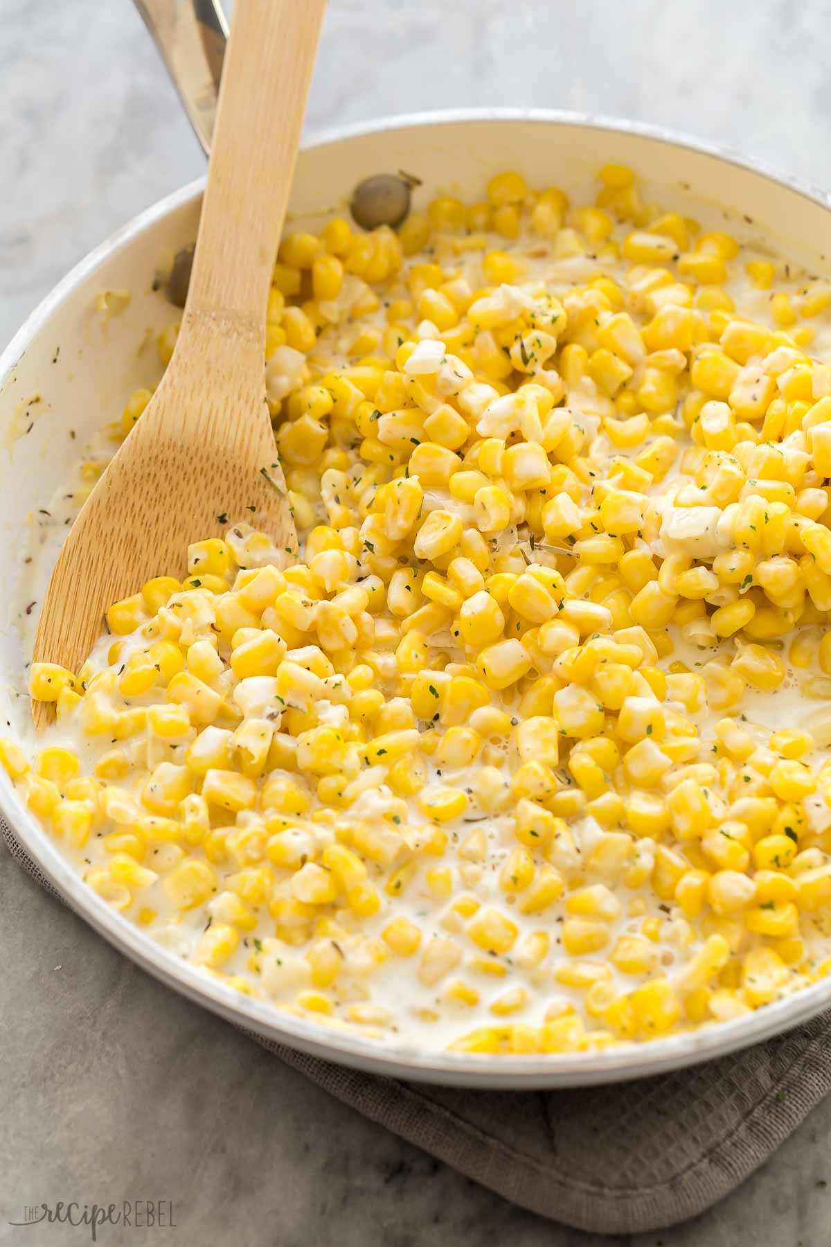 close up image of creamed corn in white skillet with wooden spoon.