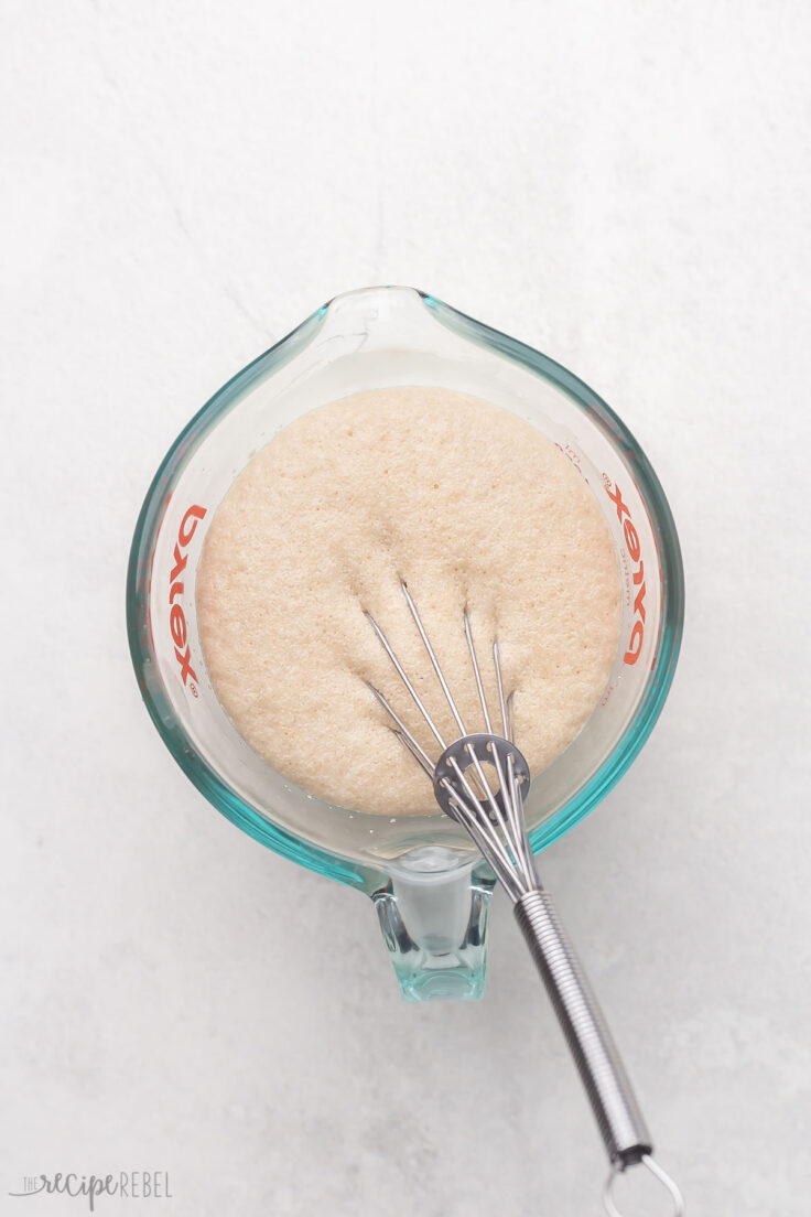 glass measuring cup with whisk and yeast.