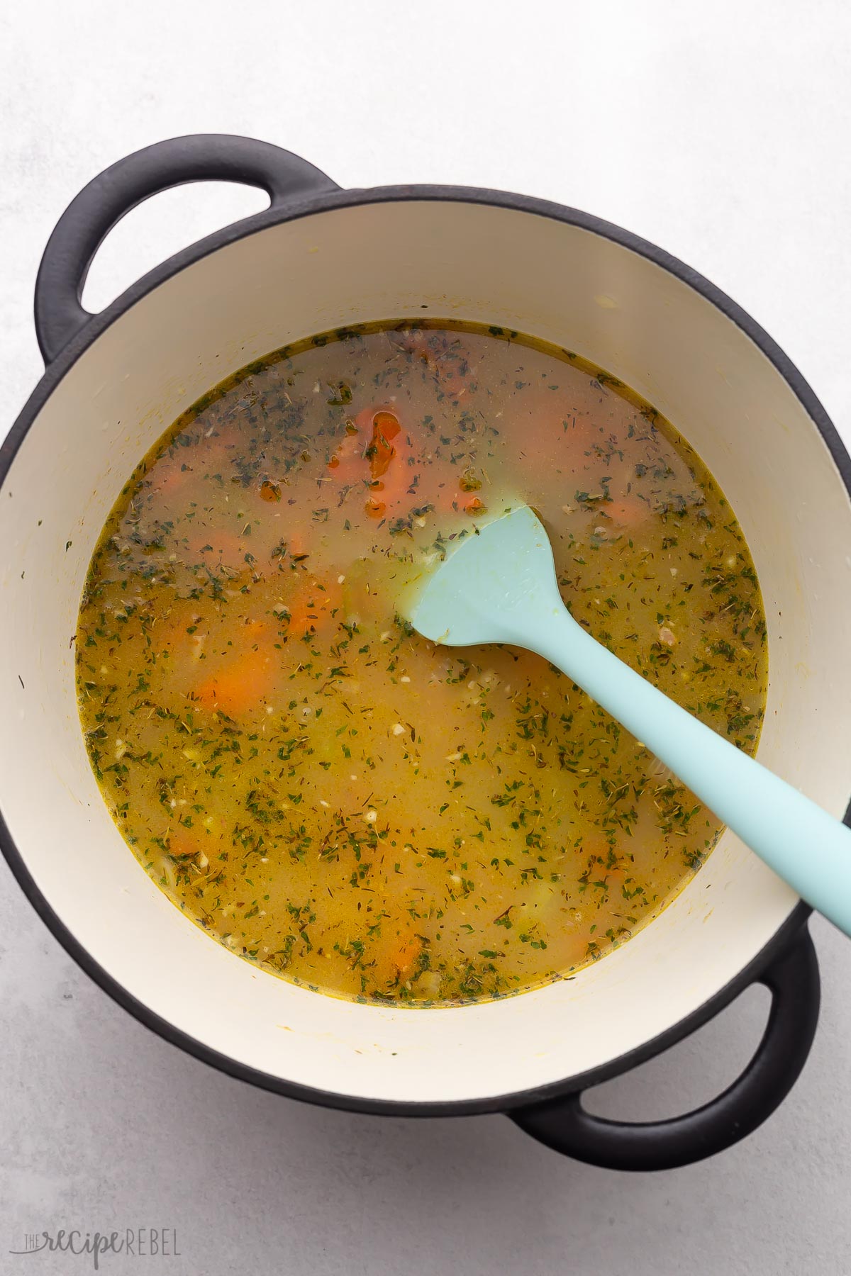 broth and vegetables in pot with blue spatula.